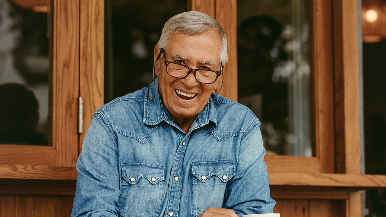 A smiling man wearing glasses enjoying a cup of coffee